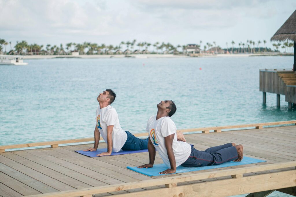 Two men practicing yoga on a deck overlooking the ocean on a sunny day.